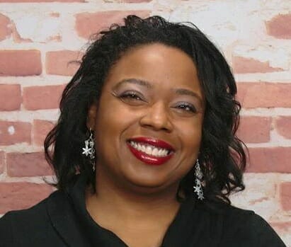 A smiling black woman with red lipstick, shoulder-length hair, and wearing a black top.