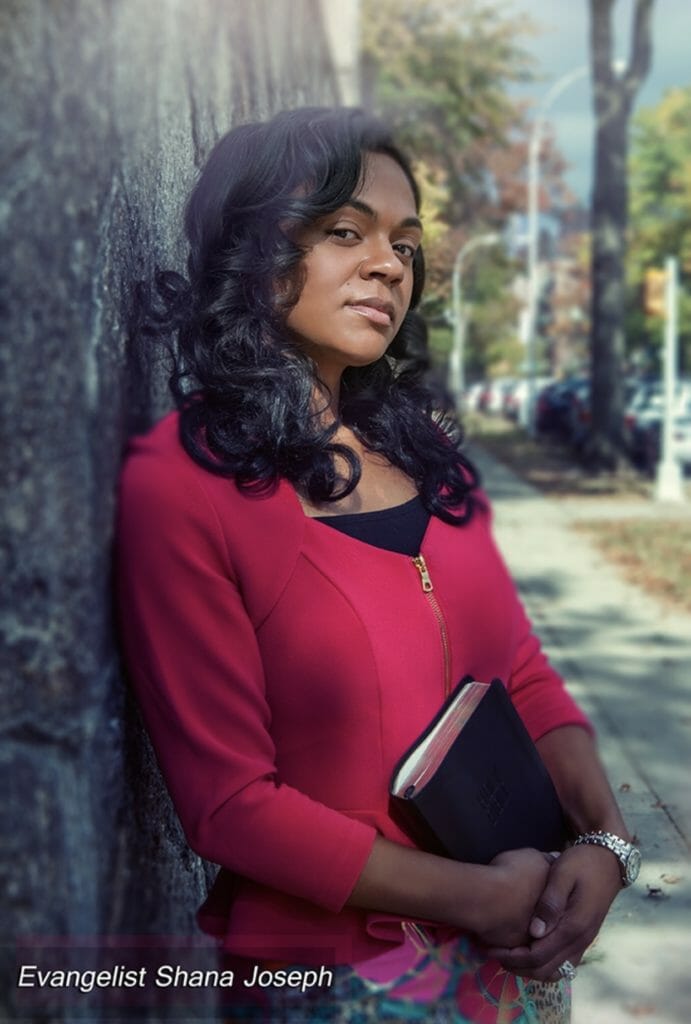 An African-American woman with long hair, wearing a red zip-up blouse and holding a Bible.