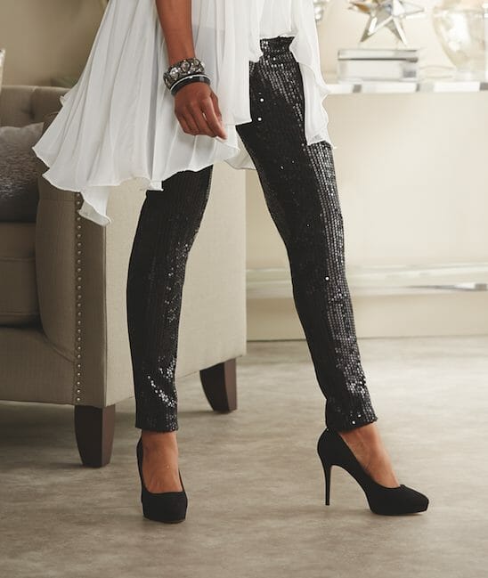 The bottom half of a woman wearing black sequin leggings and black heeled shoes.