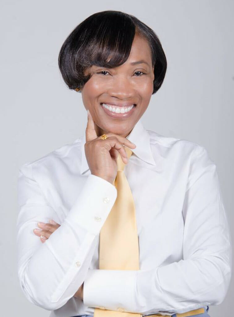 A smiling black woman with short hair and bangs, wearing a white dress shirt and light yellow tie.