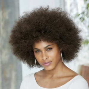 An African-American woman wearing a big dark brown Afro wig and a white top.