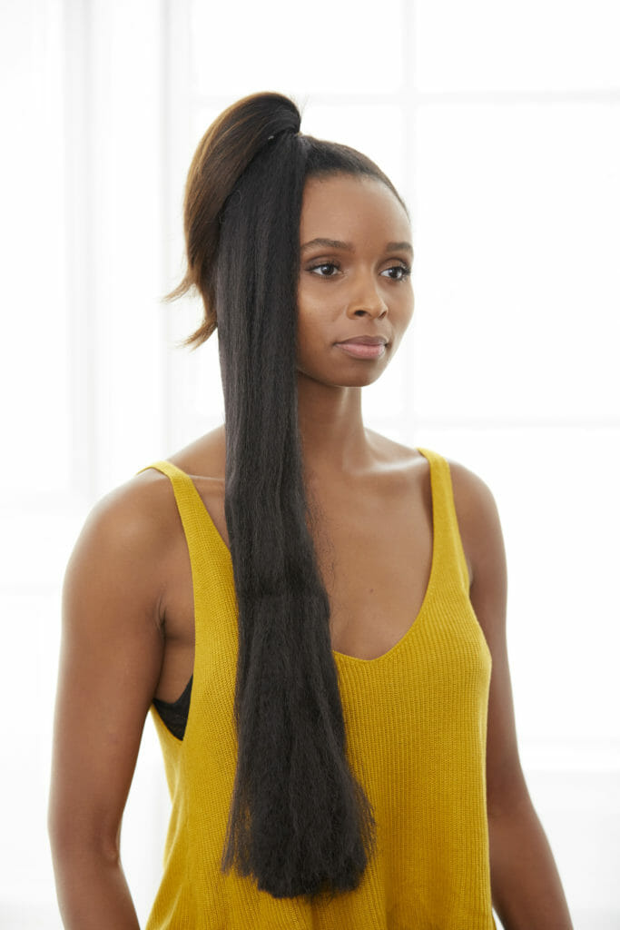 A black woman with a ponytail at the top of her head with extra braid hair attached, falling down to her chest.