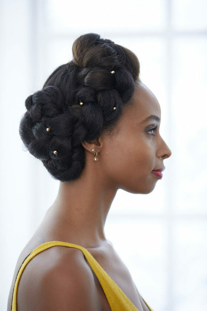 A profile of a black woman with a braided updo and hair jewelry.