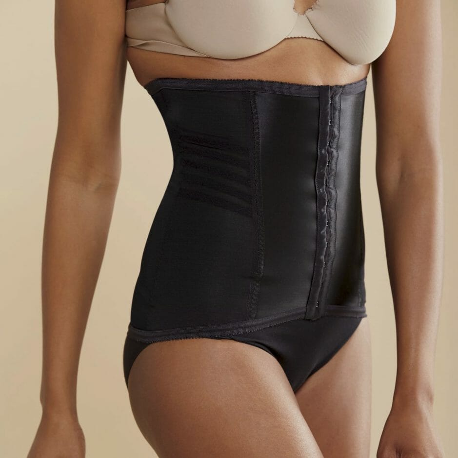 The bottom half of a black woman in a black waist cincher and a nude bra.