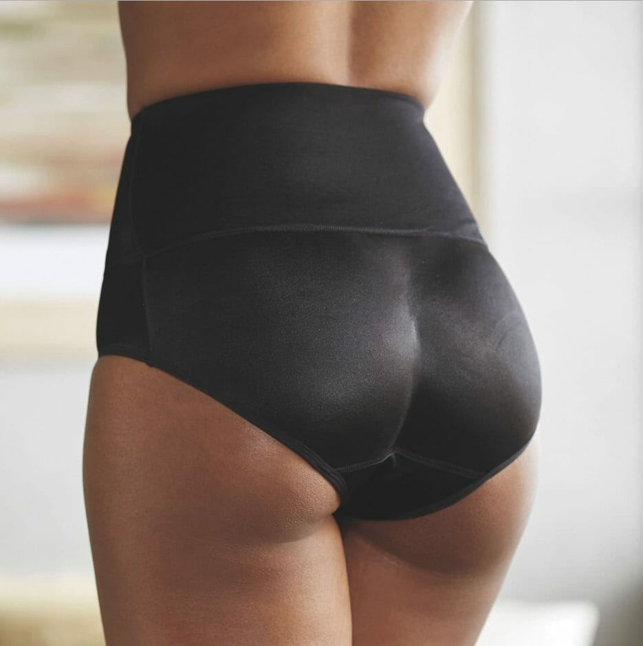 A midsection of an African-American woman in a black bottom-shaping shapewear panty.