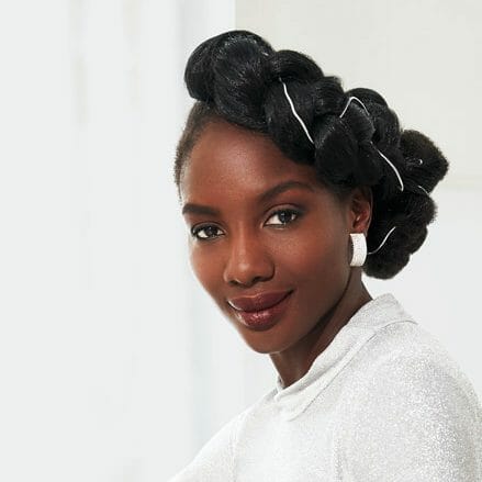 A black woman in a white top, with a fancy braid updo hairstyle.