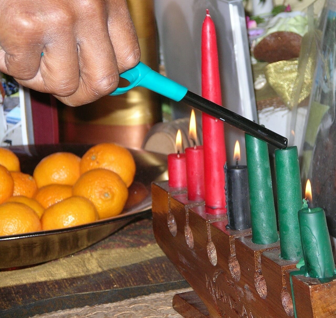 Lighting Kwanzaa candles with a stick lighter, and a dish with oranges in the background.