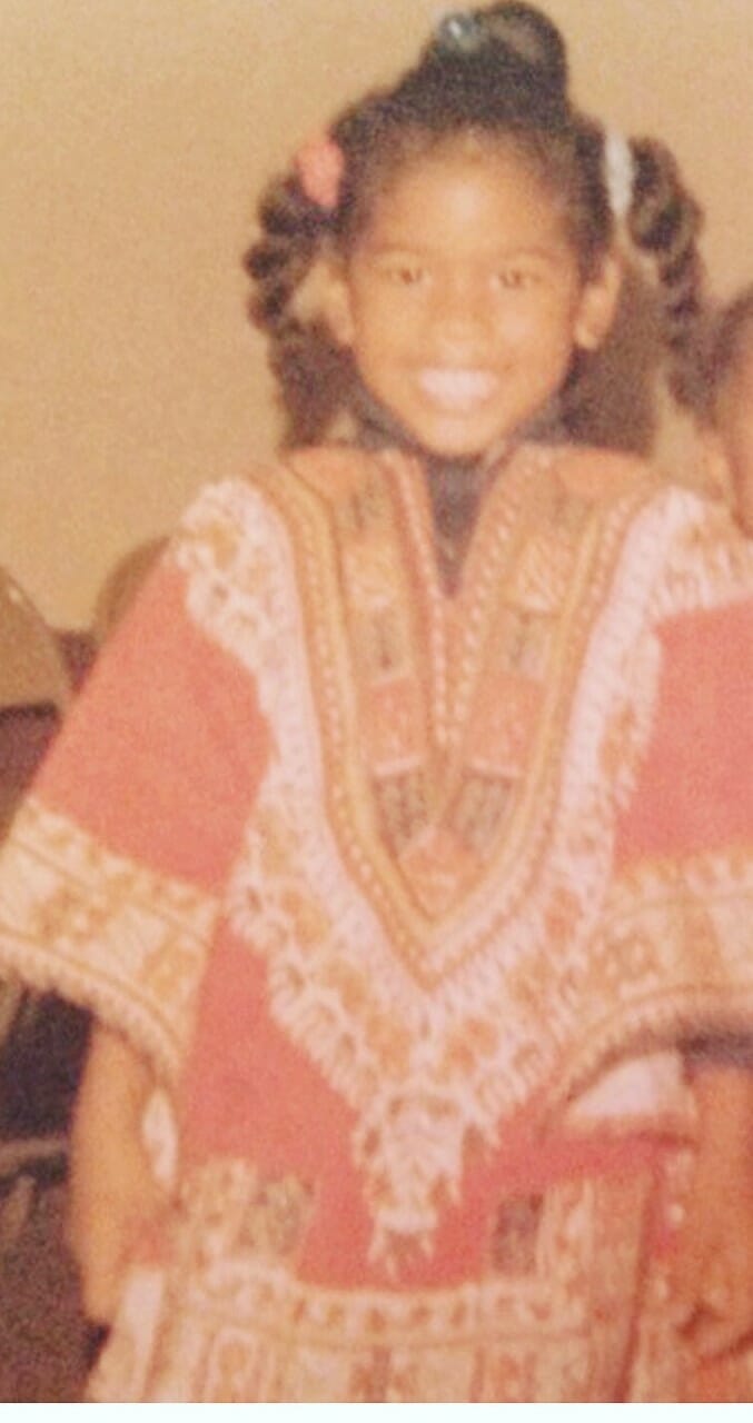 An African-American girl with pigtails wearing red Dashiki.
