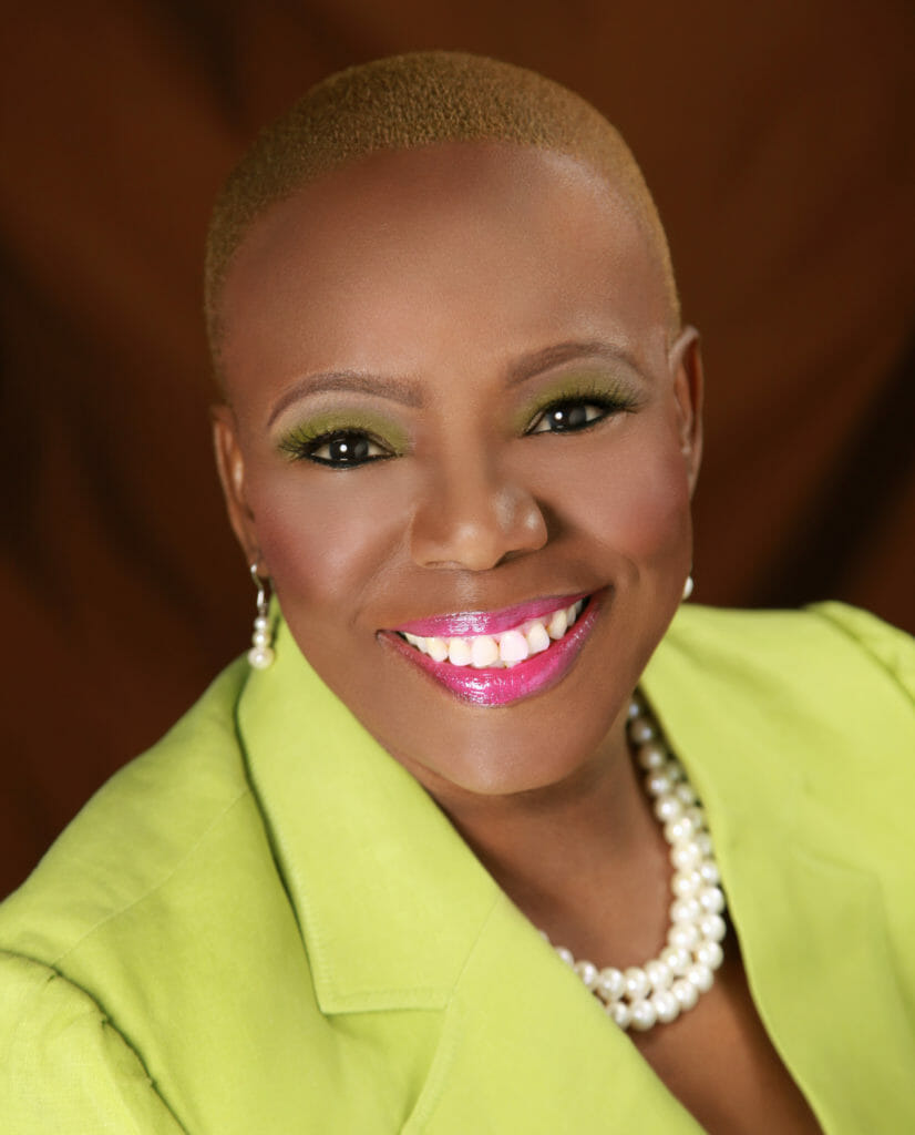 Dr. Joyce Morley, a smiling African-American woman with a shaved head, wearing a lime green suit jacket and white pearls.