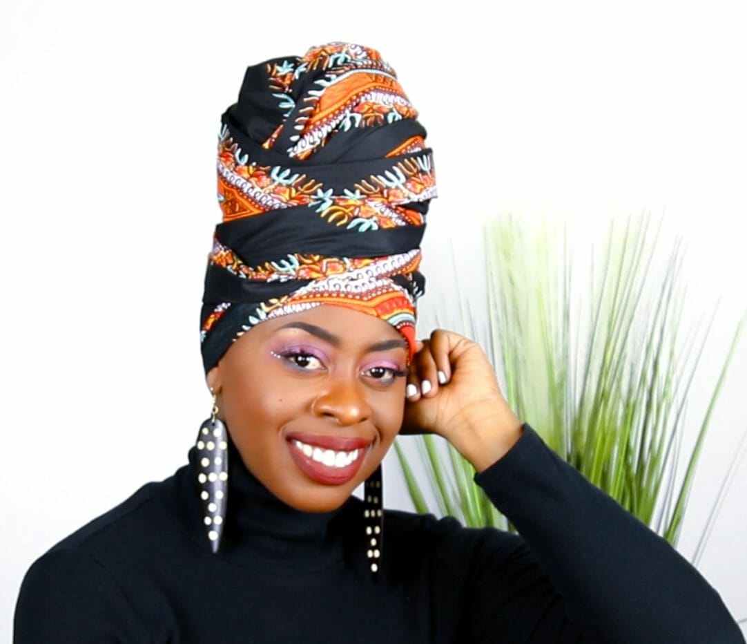A smiling African-American woman in a multi-print headwrap, wrapped high on top of head.