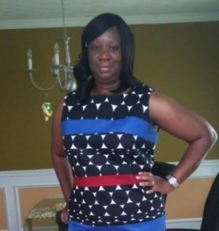A black woman with shoulder-length hair, in a black and white circle print dress with blue and red stripes.