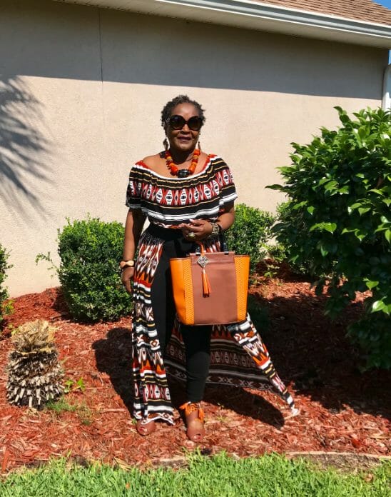 A black woman out on a sunny day, wearing a colorful, multi-print pant set with an off-the-shoulder top.