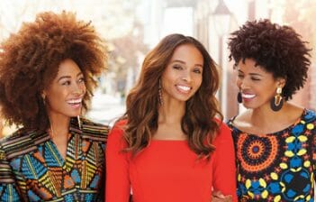 Three smiling African-American women together on a city sidewalk.