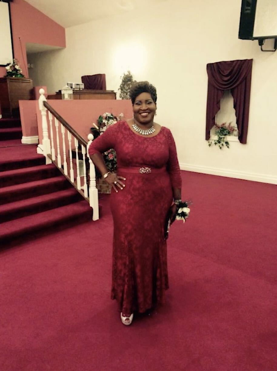 Reuben Reuel's Mother, an African-American woman in a fancy red dress with a wrist corsage in a church.