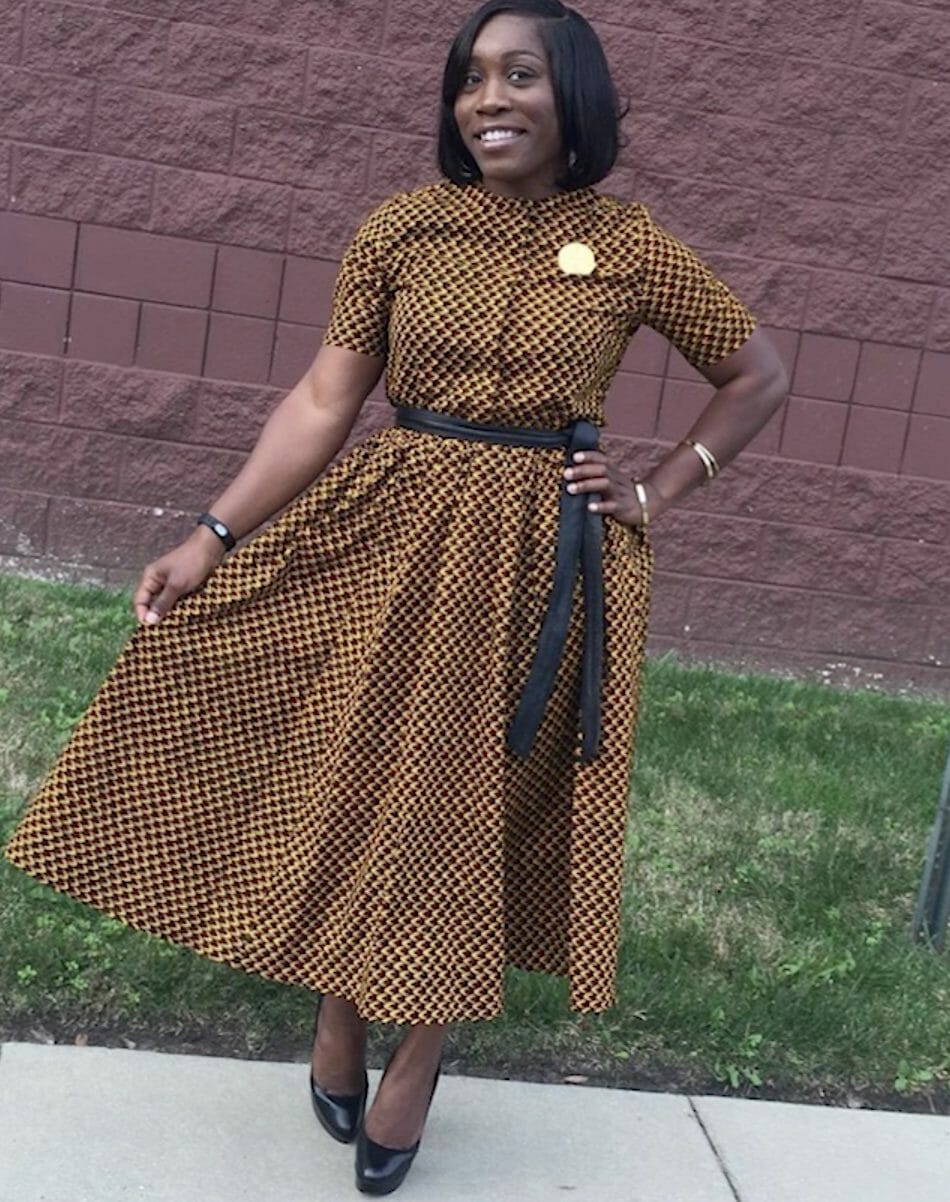 Reuben Reuel's Sister, an African-American woman in a brown houndstooth shirt dress with a flared skirt.