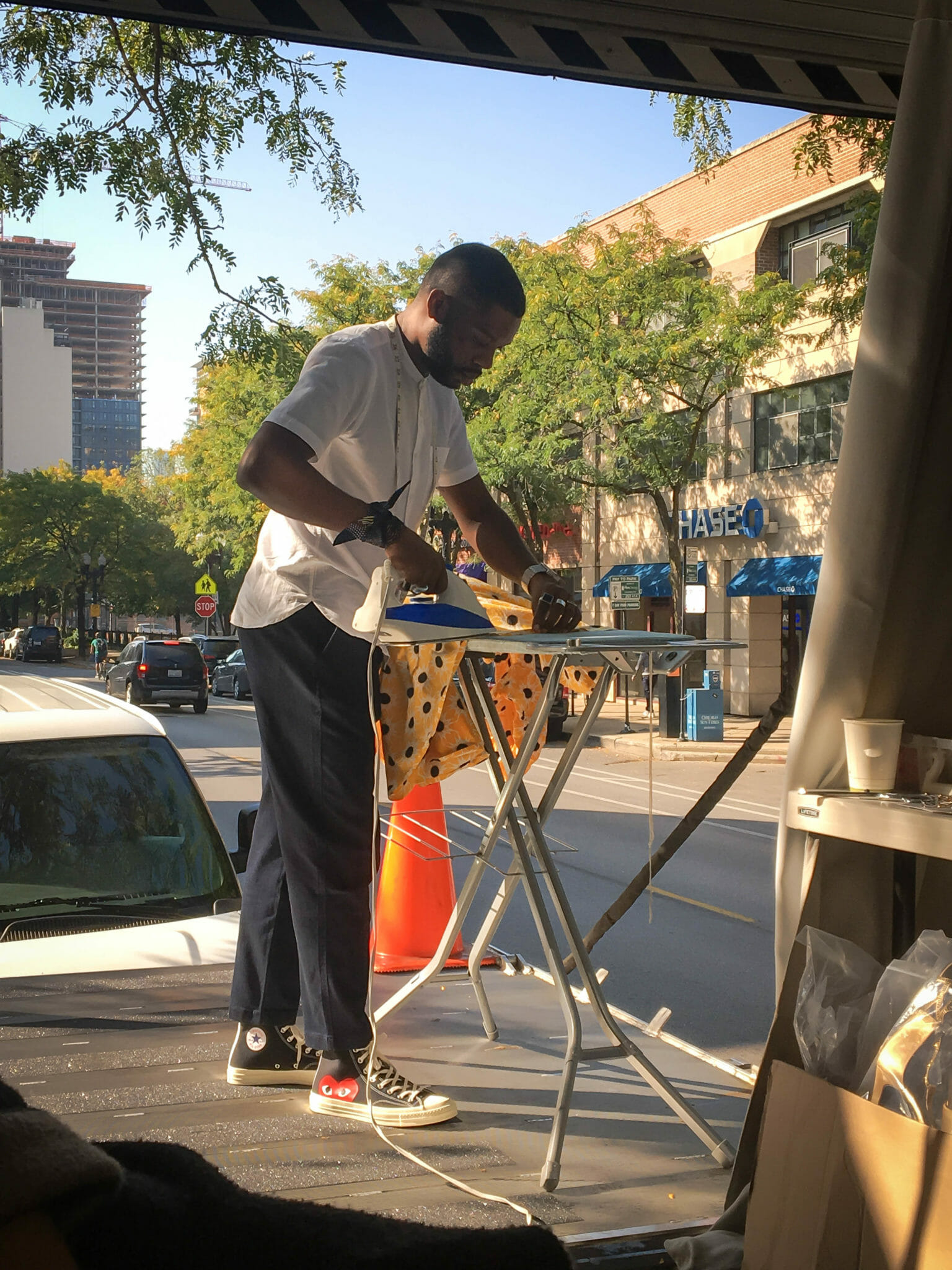 An African-American man ironing yellow sunburst print fabric on a city street.