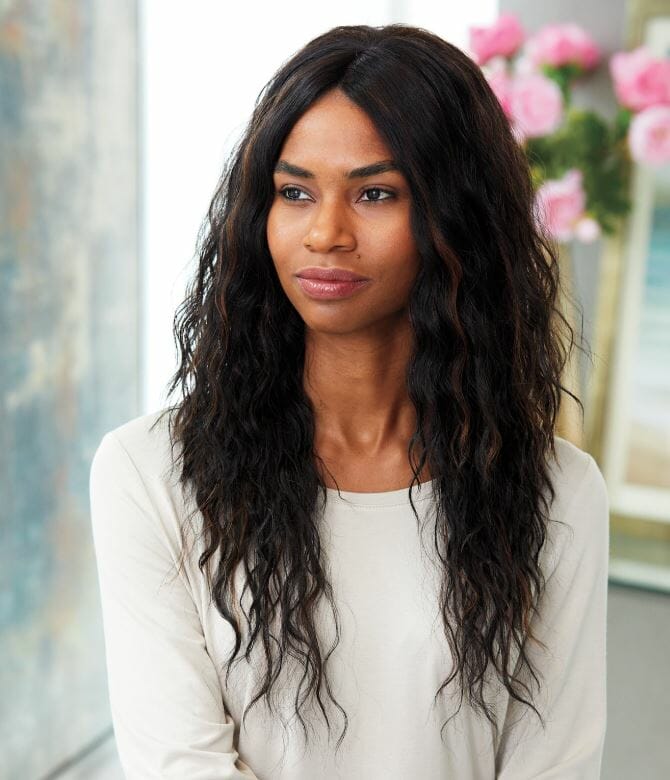 An African-American woman wearing a white top and a very long, wavy black Vivica Fox wig with a center part.