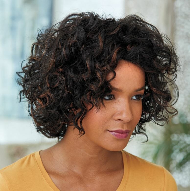 An African-American woman wearing a goldenrod top and a short, curly brown Vivica Fox wig with a side part.