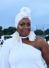 Ashro Woman of the Week, Beverly, an black woman wearing a white dress and matching headwrap at an outdoor event.