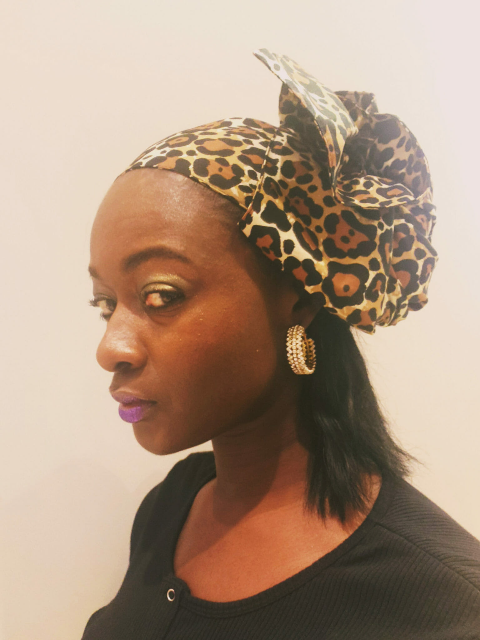An African-American woman wearing a black dress and a cheetah print headwrap and gold hoop earrings.