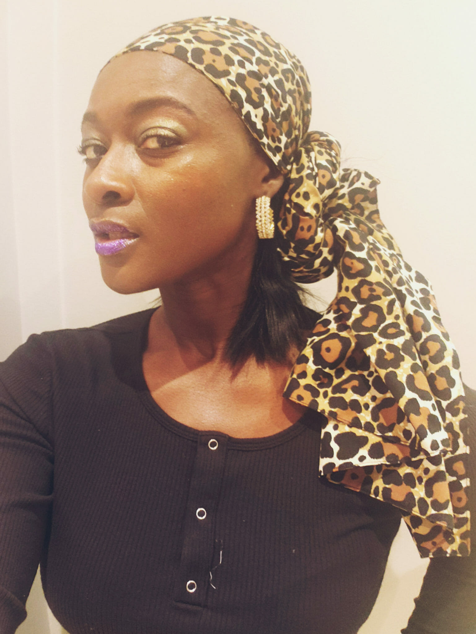 An African-American woman wearing a black dress and a cheetah print headwrap with ends on her shoulder.