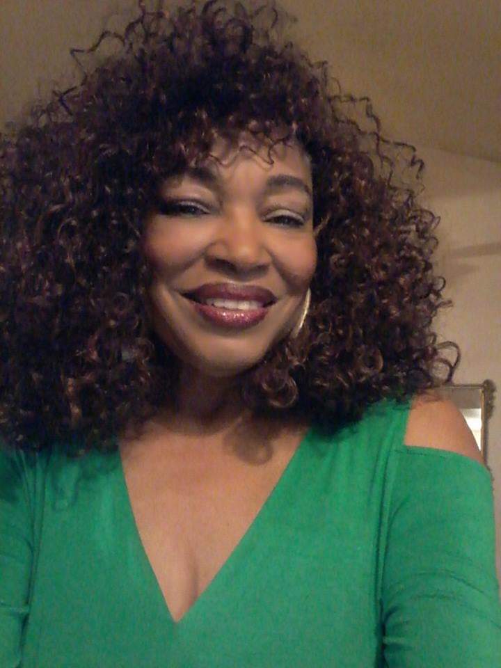 Ashro Woman of the Week, Lucy, a smiling African-American woman with full curly hair, wearing a green V-neck dress.