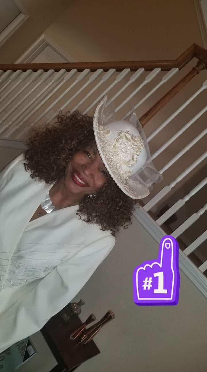 Ashro Woman of the Week, Lucy, a black woman with full curly hair, wearing a white hat and white suit.