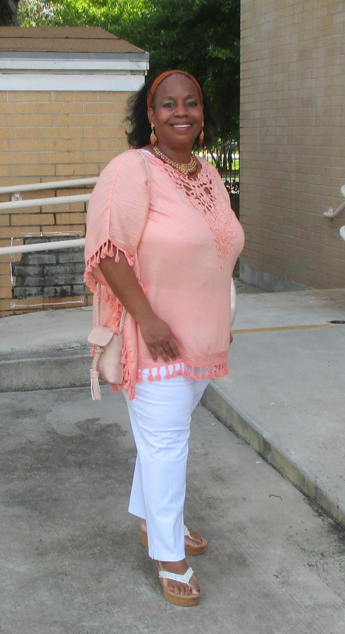 Ashro Woman of the Week, Tracey, a smiling African-American woman in a summery coral top and white slacks.