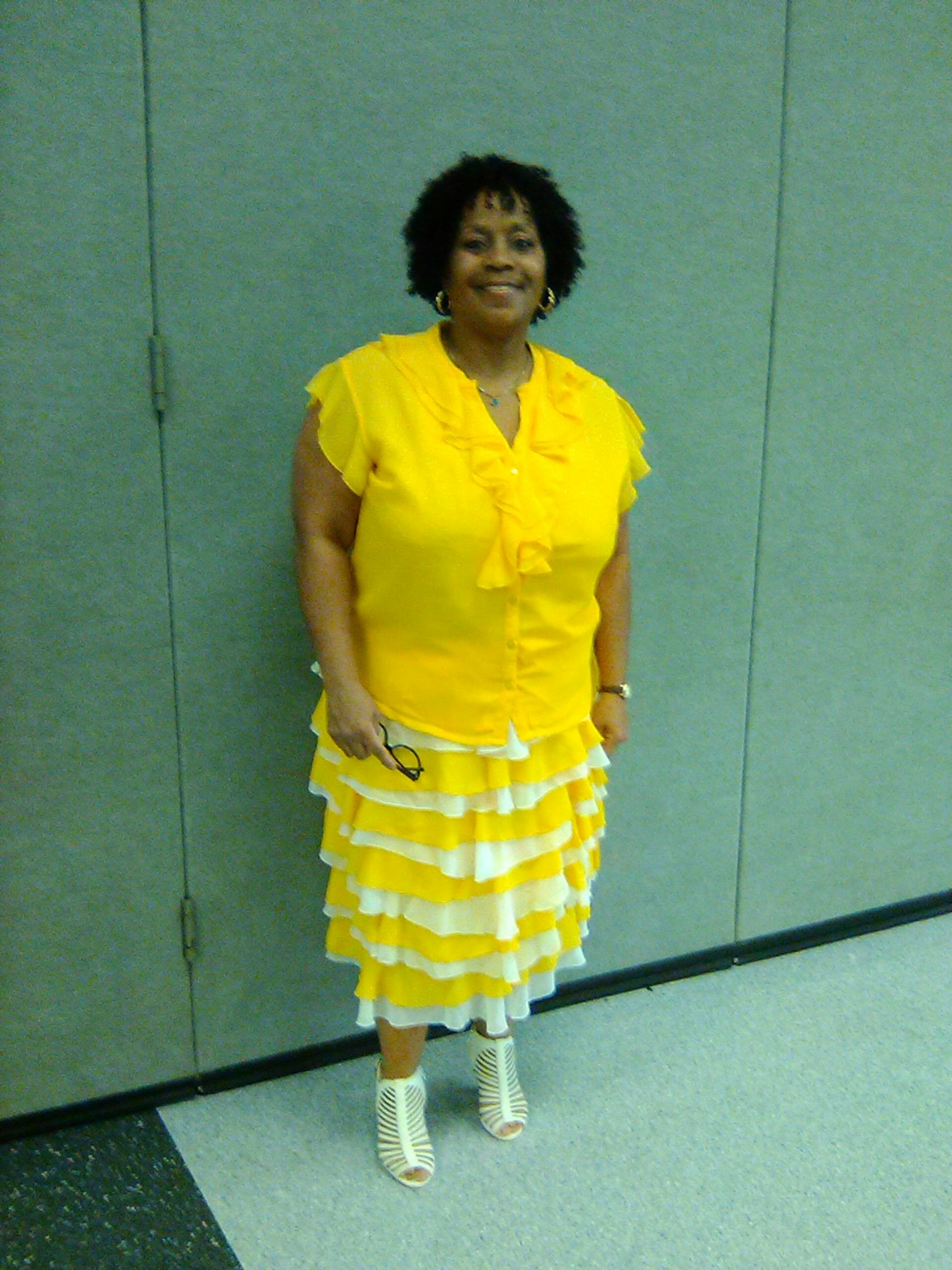 Ashro Woman of the Week, Tracey, a black woman in a bright yellow short-sleeve blouse and ruffled skirt.