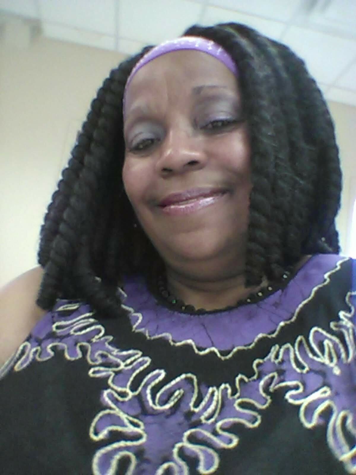 Ashro Woman of the Week, Tracey, a black woman with shoulder-length curly hair, in a black and lavender top.