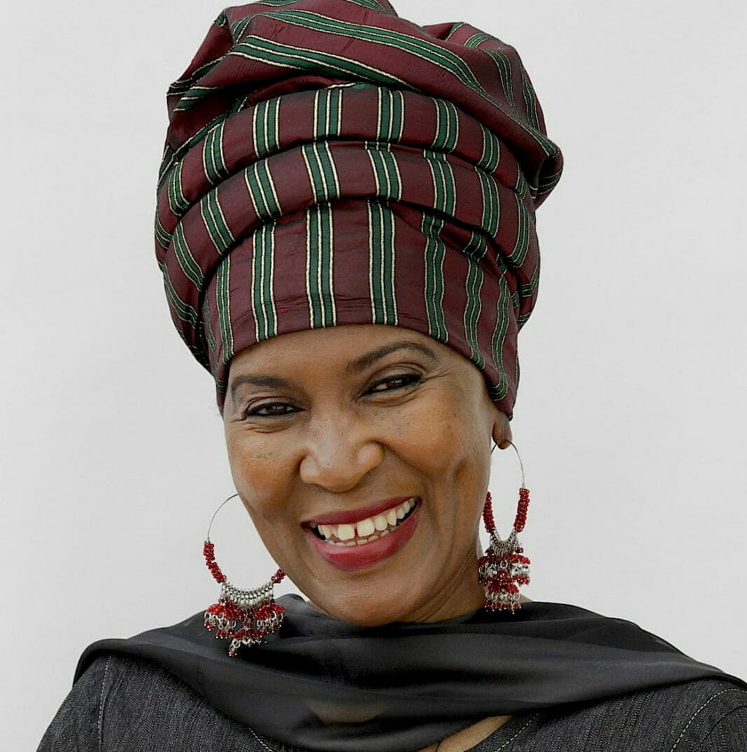 Ashro Woman of the Week, Wajeedah, a smiling black woman in a gray print headwrap and gray buttoned coat.