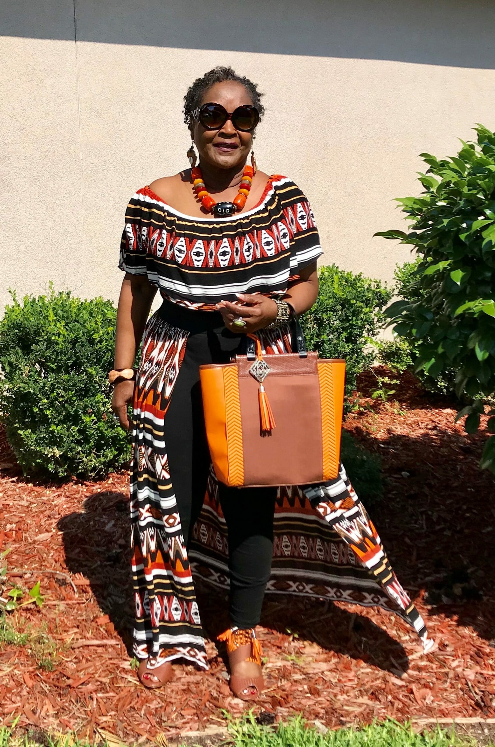 Ashro Woman of the Week, Dianne F., a black woman wearing an off-the-shoulder print dress and red necklace.