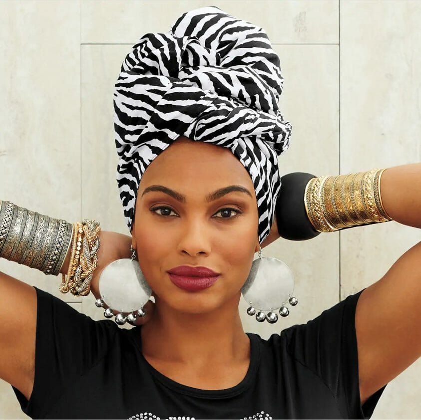 An African-American woman wearing a black and white zebra print headwrap, black dress, and metal cuff bracelets.