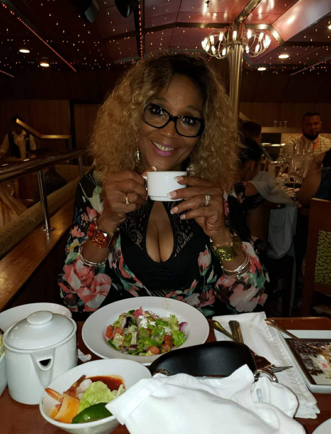 Ashro Woman of the Week CAROLYN, a smiling blonde African-American woman in glasses enjoying a restaurant dinner.