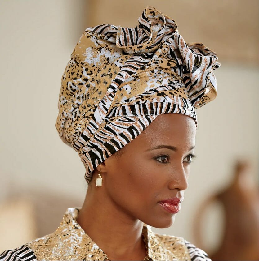 An African-American woman wearing a gold, black and white animal print headwrap and matching outfit.