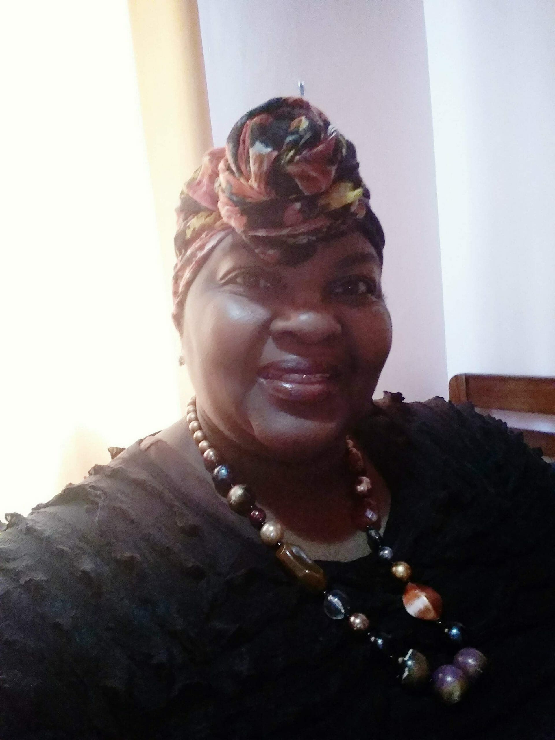 Ashro Woman of the Week Brenda, a smiling African-American woman wearing a black dress and a floral headwrap