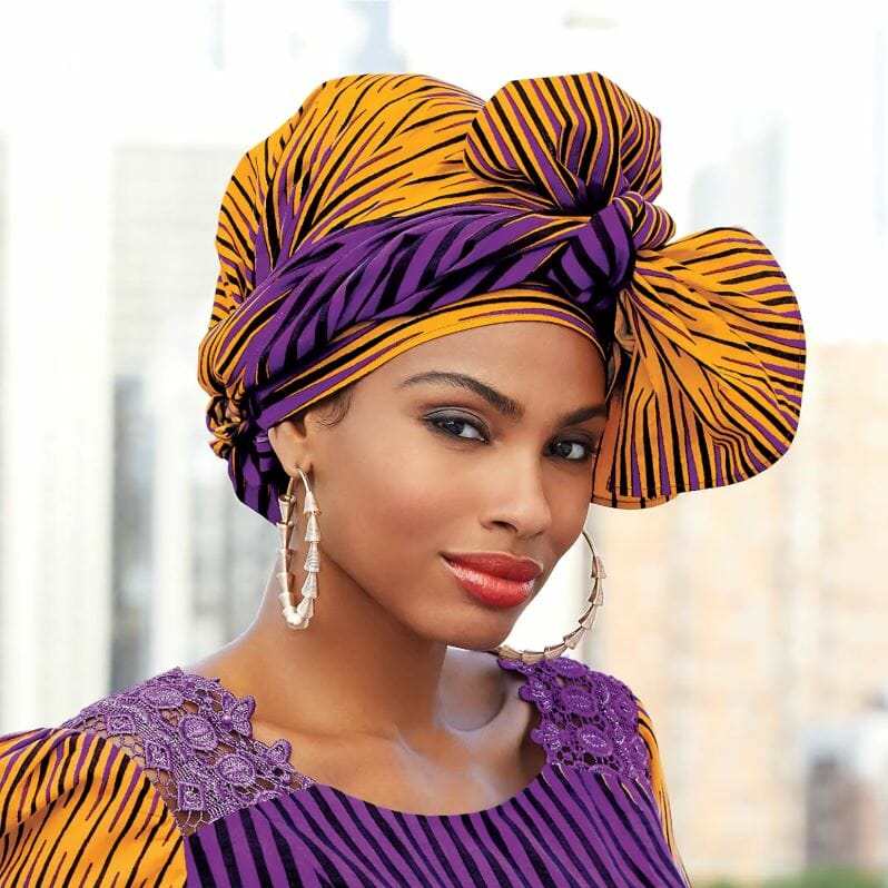 An African-American woman wearing a gold and purple headwrap, matching dress, and hoop earrings.