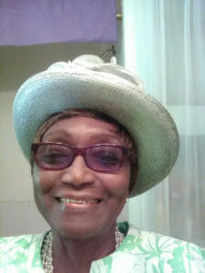 Ashro Woman of the Week Ruth, a smiling African-American woman wearing a green floral dress and hat.