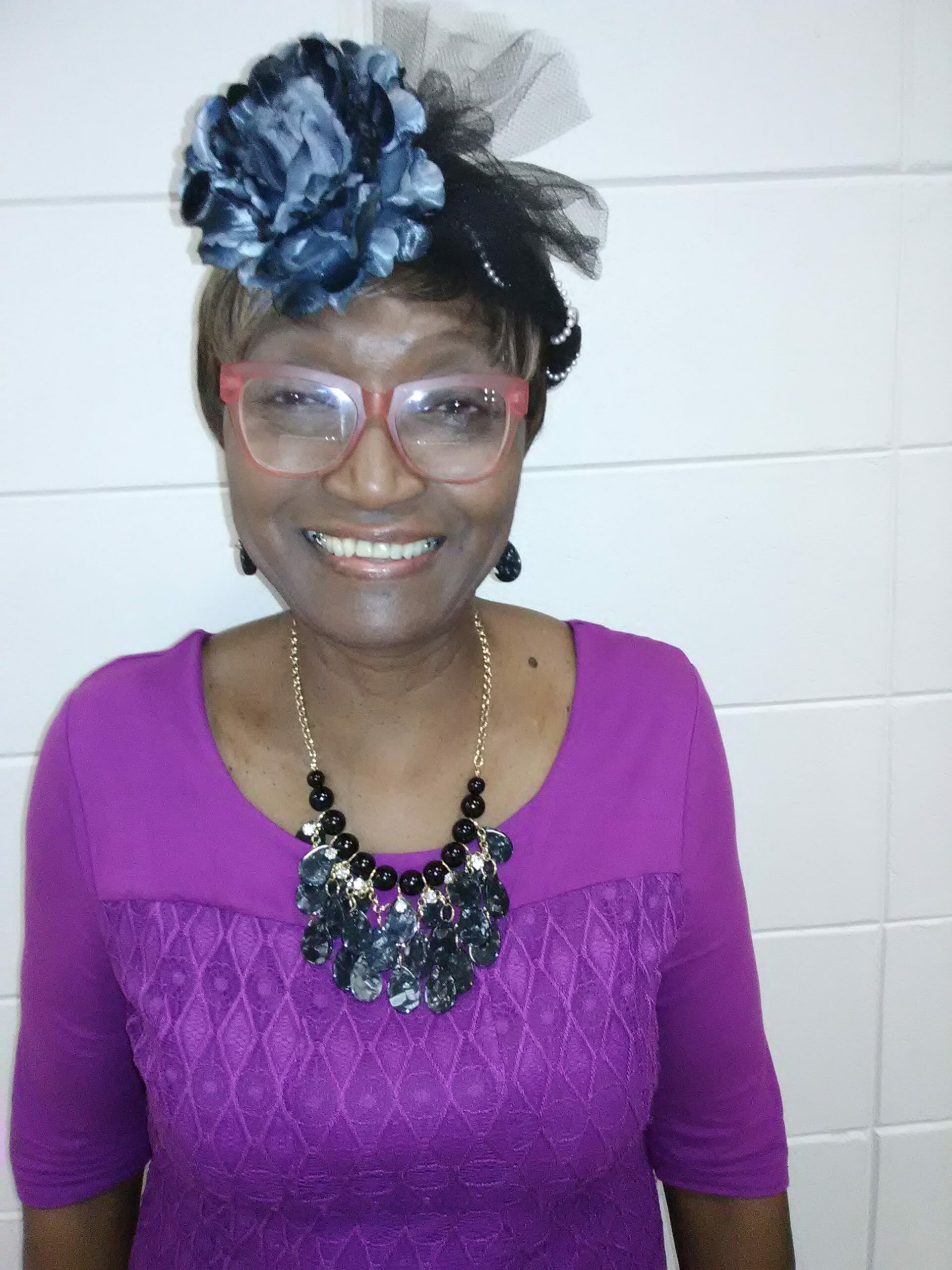 Ashro Woman of the Week Ruth, a smiling African-American woman wearing a purple dress and hat.