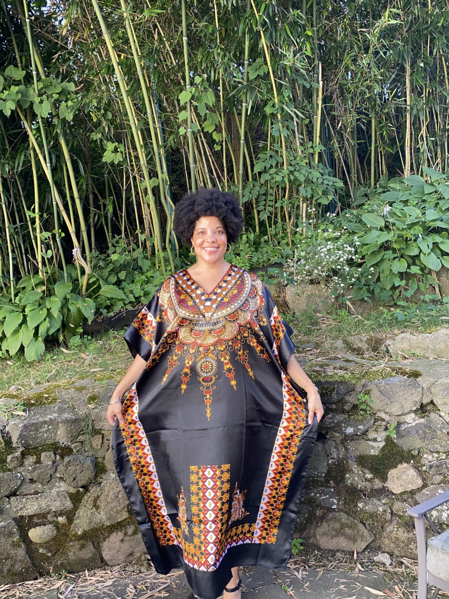 A black woman wearing a black and orange and Afrocentric patterned caftan.