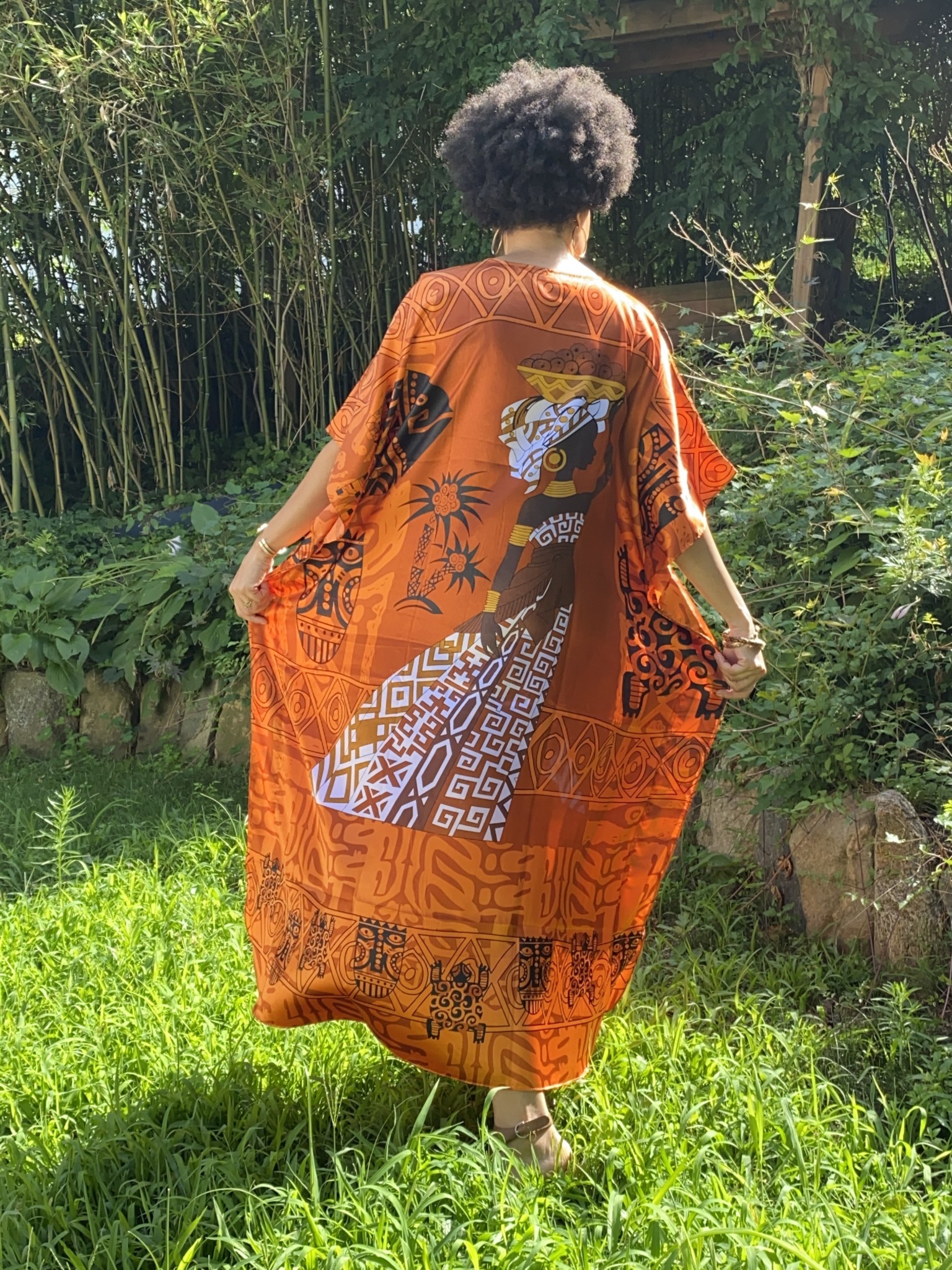 A black woman wearing an orange and Afrocentric patterned caftan.