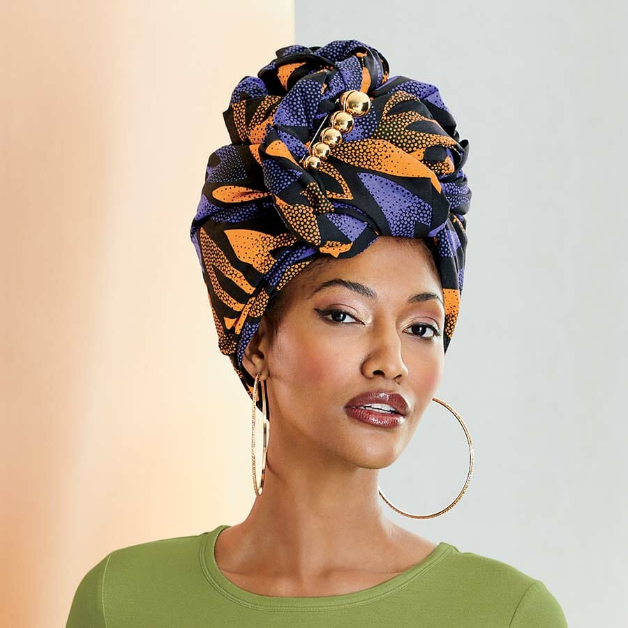 African American woman wearing purple, orange and black headwrap with gold earrings and green shirt.