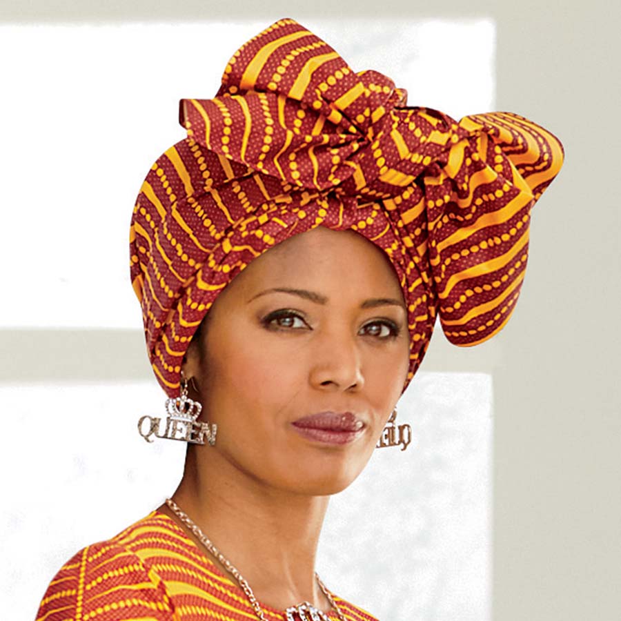 African American woman wearing a gold and orange headwrap, matching top, and crown queen earrings