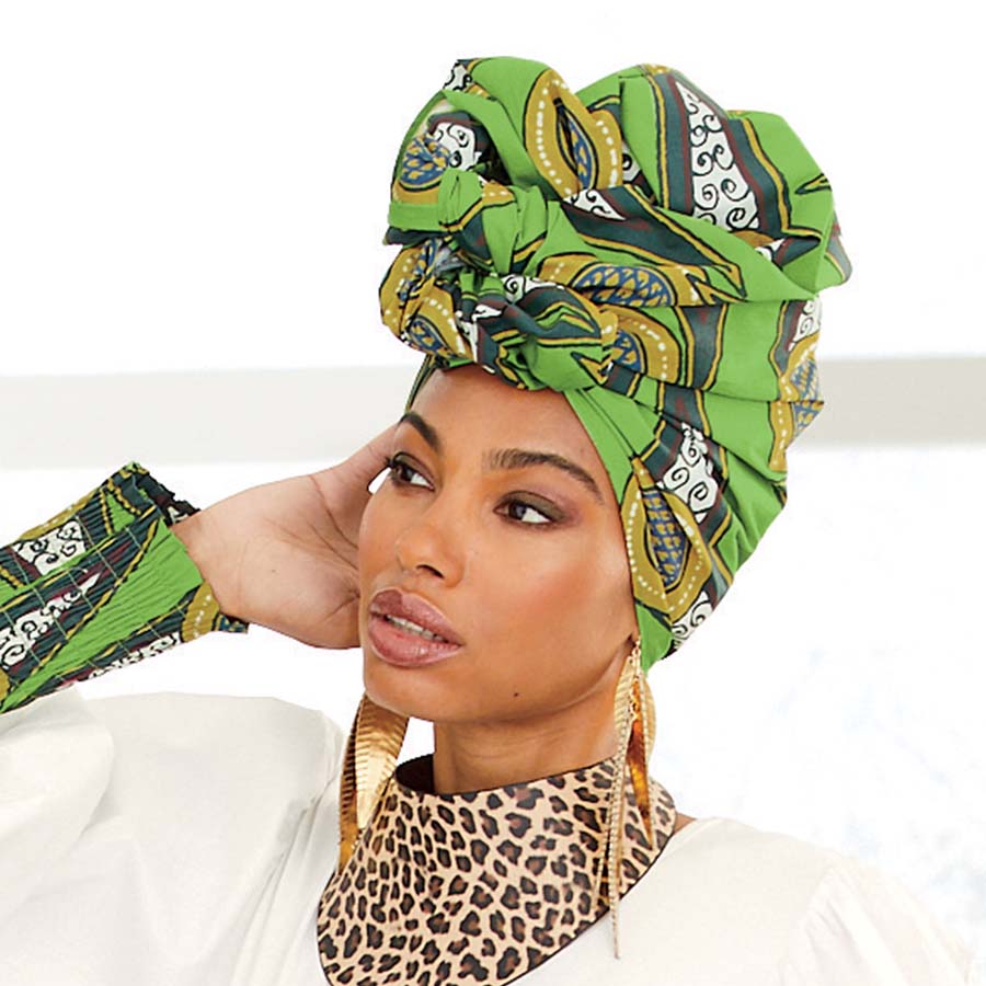 African American woman wearing a green, brown, black and white print headwrap and matching dress with drop earrings and leopard print necklace.