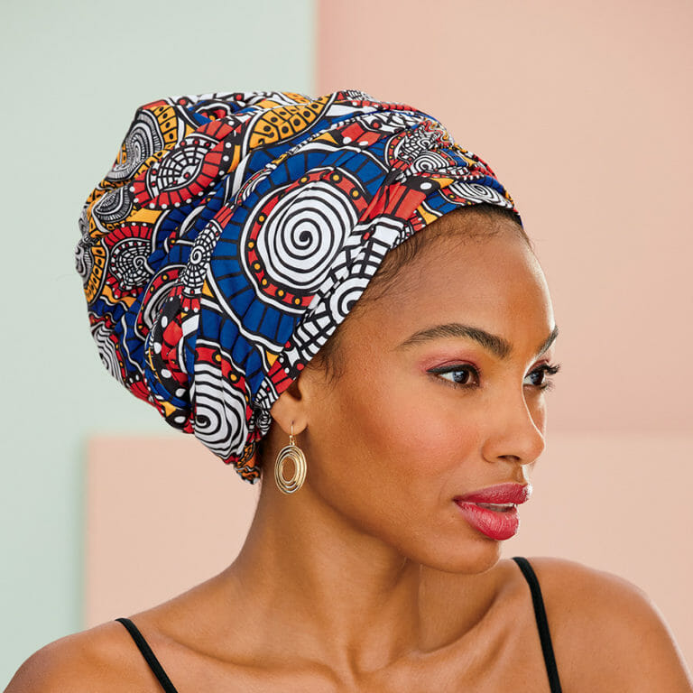 African American woman with red, blue, yellow, black and white print headwrap and circular gold earrings with black top.