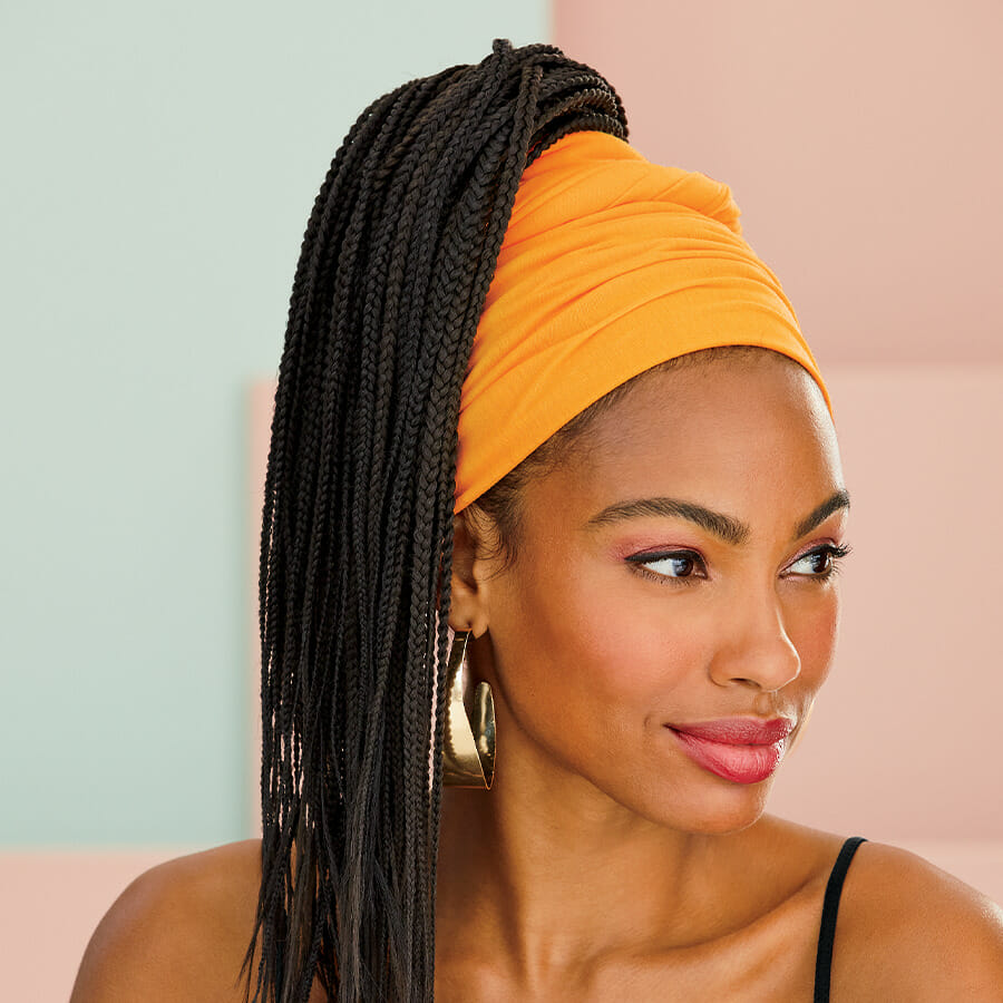 African American woman with long dark braids, yellow headrap and thick gold hoop earrings.
