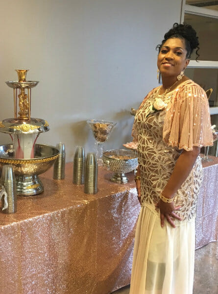 Black woman in a nice outfit in front of a punch bowl.