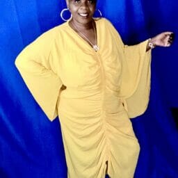 Black woman wearing yellow dress and blue headwrap.