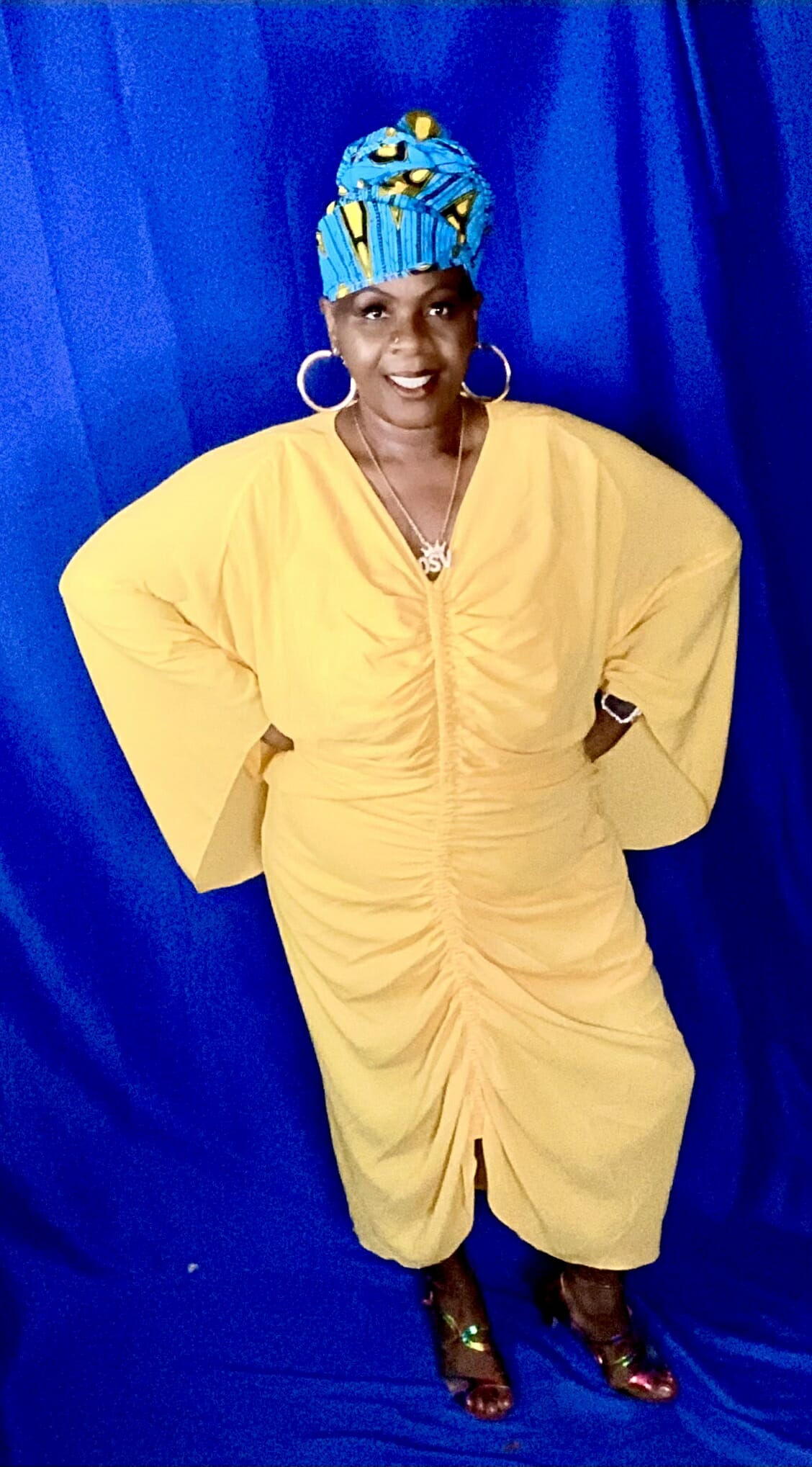 Black woman wearing yellow dress and blue headwrap.