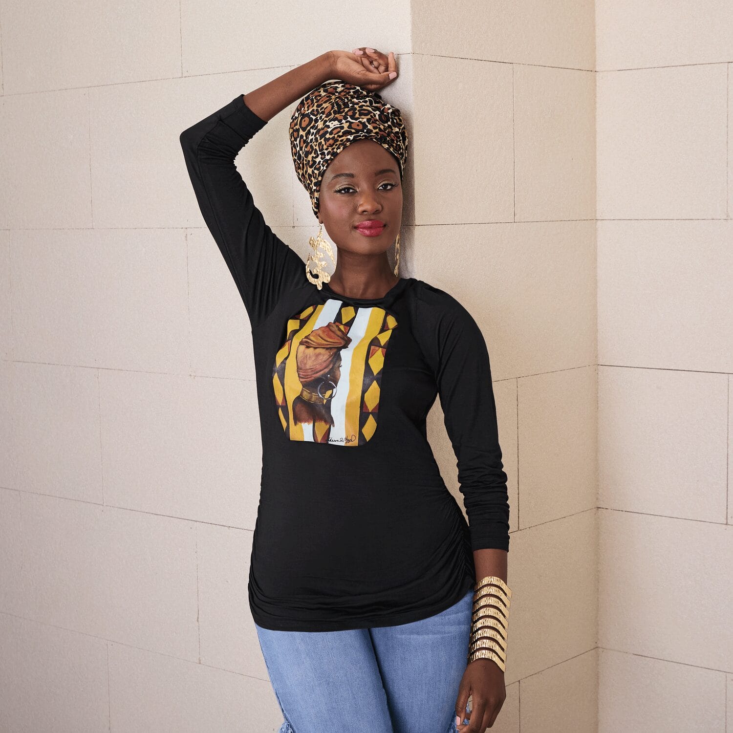 A Black woman wearing a black shirt featuring artwork of a Black woman facing away, showing only her headwrap and earrings